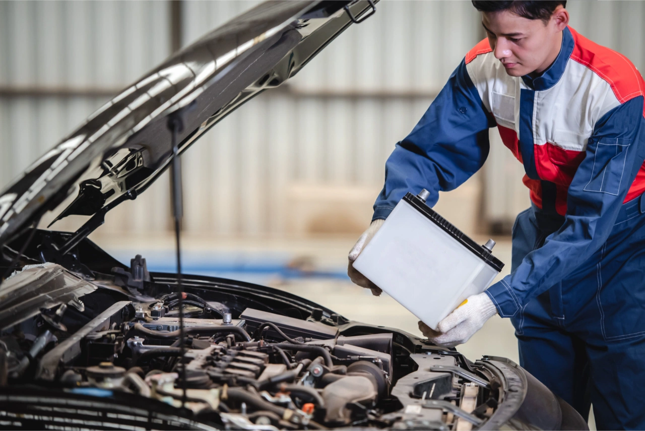 Technicien remplaçant une batterie de voiture dans un atelier Peugeot.