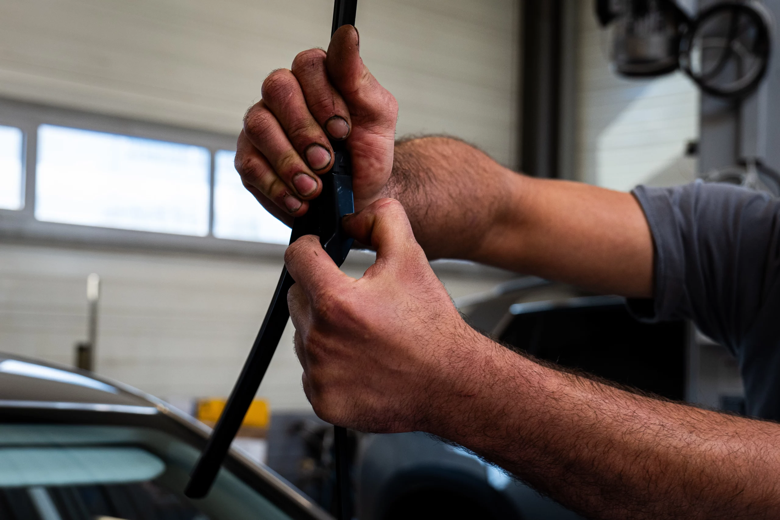 Essuie-glace d'un véhicule Peugeot en gros plan sur les mains d'un mécanicien entrain de les changer.